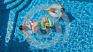 Family in swimming pool aerial drone view from above, happy mother and kids swim on inflatable ring donuts and have fun in water