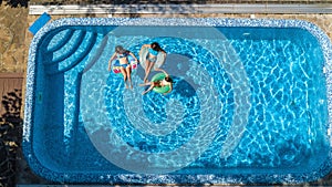 Family in swimming pool aerial drone view from above, happy mother and kids swim on inflatable ring donuts and have fun in water