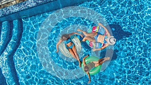 Family in swimming pool aerial drone view from above, happy mother and kids swim on inflatable ring donuts and have fun in water