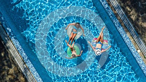 Family in swimming pool aerial drone view from above, happy mother and kids swim on inflatable ring donuts and have fun in water