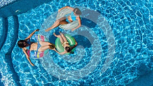 Family in swimming pool aerial drone view from above, happy mother and kids swim on inflatable ring donuts and have fun in water