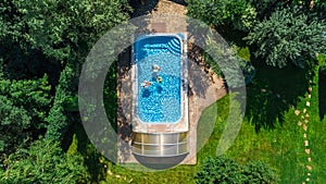 Family in swimming pool aerial drone view from above, happy mother and kids swim on inflatable ring donuts and have fun in water