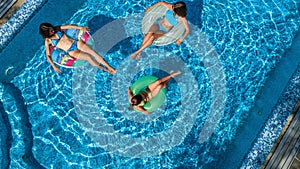 Family in swimming pool aerial drone view from above, happy mother and kids swim on inflatable ring donuts and have fun in water