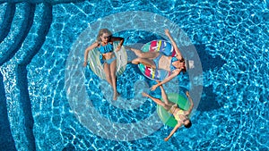 Family in swimming pool aerial drone view from above, happy mother and kids swim on inflatable ring donuts and have fun in water