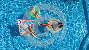 Family in swimming pool aerial drone view from above, happy mother and kids swim on inflatable ring donuts and have fun in water