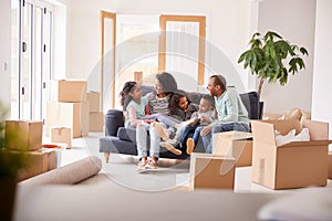 Family Taking A Break And Sitting On Sofa Celebrating Moving Into New Home Together