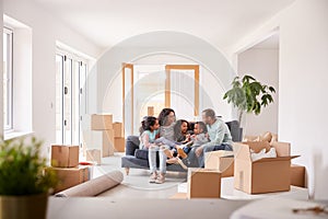 Family Taking A Break And Sitting On Sofa Celebrating Moving Into New Home Together