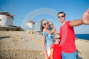 Family taking selfie with a stick in front of windmills at popular tourist area on Mykonos island, Greece