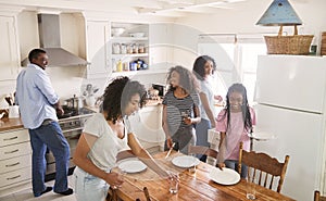 Family With Teenage Daughters Laying Table For Meal In Kitchen