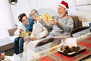 Family with teenager and grandfathers sitted at the sofa at home the morning of christmas laughing and openening their presents