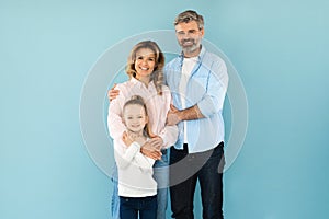 Family Of Three Embracing Smiling Standing On Blue Background