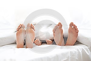 Family of three hiding under blanket with bare feet outside