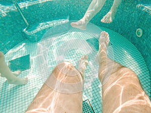 Family of three in hot tub, underwater shot of legs in bubbly pool water