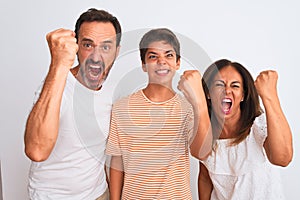 Family of three, mother, father and son standing over white isolated background angry and mad raising fist frustrated and furious