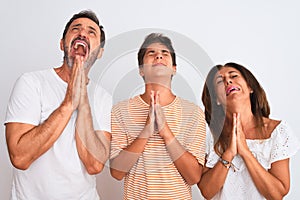 Family of three, mother, father and son standing over white isolated background begging and praying with hands together with hope