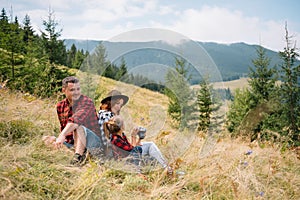 Rodina tří lidí odpočívá v horách. Po náročném výstupu na horu se posadili k odpočinku, napili se vody