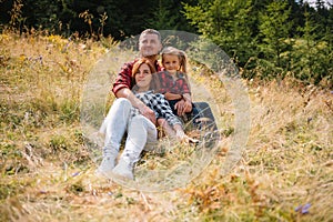 Family of three people rest in the mountains. They sat down to rest, drink water after a hard climb to the mountain