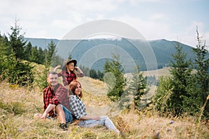 Rodina tří lidí odpočívá v horách. Po náročném výstupu na horu se posadili k odpočinku, napili se vody