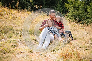 Family of three people rest in the mountains. They sat down to rest, drink water after a hard climb to the mountain