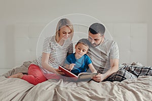 Family of three people sitting on bed in bedroom reading book