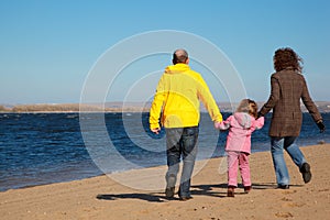 Family of three people walking along beach.