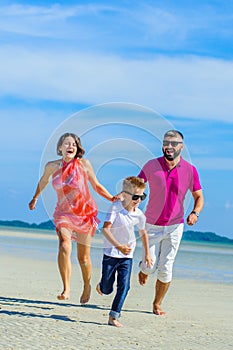 Family of three running along the tropical beach, laughing and enjoing time together.