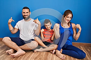 Family of three sitting on the floor at home looking confident with smile on face, pointing oneself with fingers proud and happy