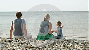 Family of three sitting on pebble beach by the