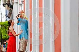 A family of three standing behind the wall outside.