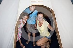 Family of three are standing into tepee in photo