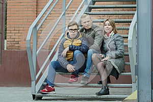 Family of three street urban portrait sitting on metal stairs at brick building background