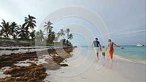 Family of three walking along the beach in tropics