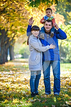 Family of three walks in the autumn park holding hands. happy father carrying son with maple leaves. Mother embrace her cute boy