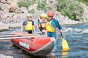 Family of three wearing life vests and helmets going to row an inflatable catamaran