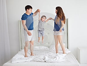 Family of three, young parents and a little son jumping and having fun in bed