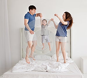 Family of three, young parents and a little son jumping and having fun in bed