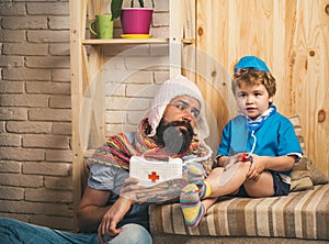 Family time, bearded man with serious boy playing doctor. Dad looks at kid dressed like male nurse with stethoscope. Man