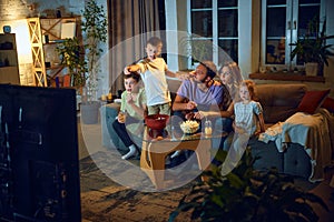 Family time. Man, woman and children watching Tv together at home in evening. Boy discussing movie scene with mother and