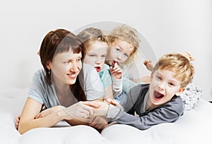 Family time: Mom and three children lie on a white bed, hugging and laughing cheerfully
