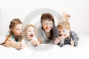 Family time: Mom and three children lie on a white bed, hugging and laughing cheerfully.