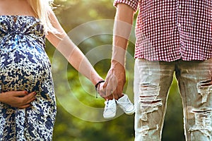 Family together holding baby shoes in hands and standing the summer park. Woman is pregnant.