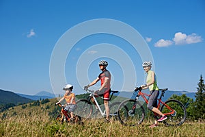 Family tourist cyclists, mother, father and child resting with bicycles on the top of grassy hill