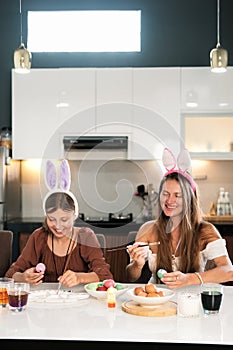 Family traditions. Mom and daughter with bunny ears decorate Easter eggs.