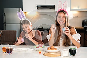 Family traditions. Mom and daughter with bunny ears decorate Easter eggs.