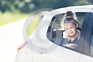 Family travel concept by car. Happy smiling child girl looking from the car window with blurred road. Summer background