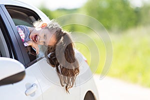 Family travel concept by car. Happy smiling child girl looking from the car window. Summer background. Soft focus