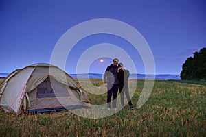 Family traveling and camping, twilight, posing near tent. Beautiful nature - field, forest, stars and moon. Father, son and girl