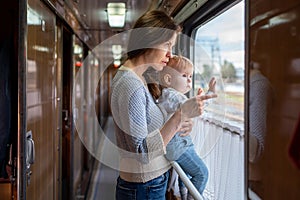 Family traveling in a train and looking through window. Mom shows his baby something outside window.