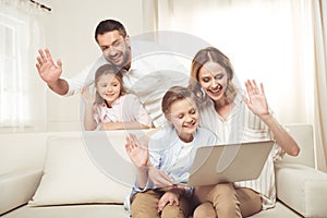 Family with two adorable children sitting together and using laptop at home