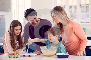 Family With Two Children In Kitchen At Home Having Fun Baking Cakes Together